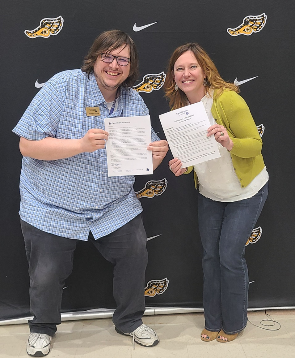 Jared Stratton and Lori Christmas stand close and hold out acceptance letters for the camera to view, smiles on their face.