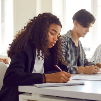 Two students sitting at a table taking notes in class