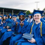 A row seated of graduates smile for the camera while holding their diplomas during the commencement ceremony