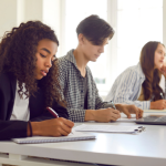 Three students take lecture notes in a bright classroom