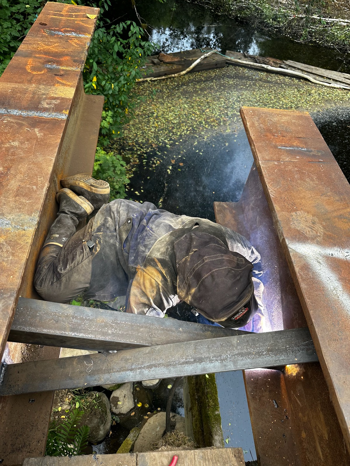 Andrew Benson working on the underside of a metal beam, the picture is taken from an artistic angle so the sparks coming off the equiptment seem to leave in an arch.