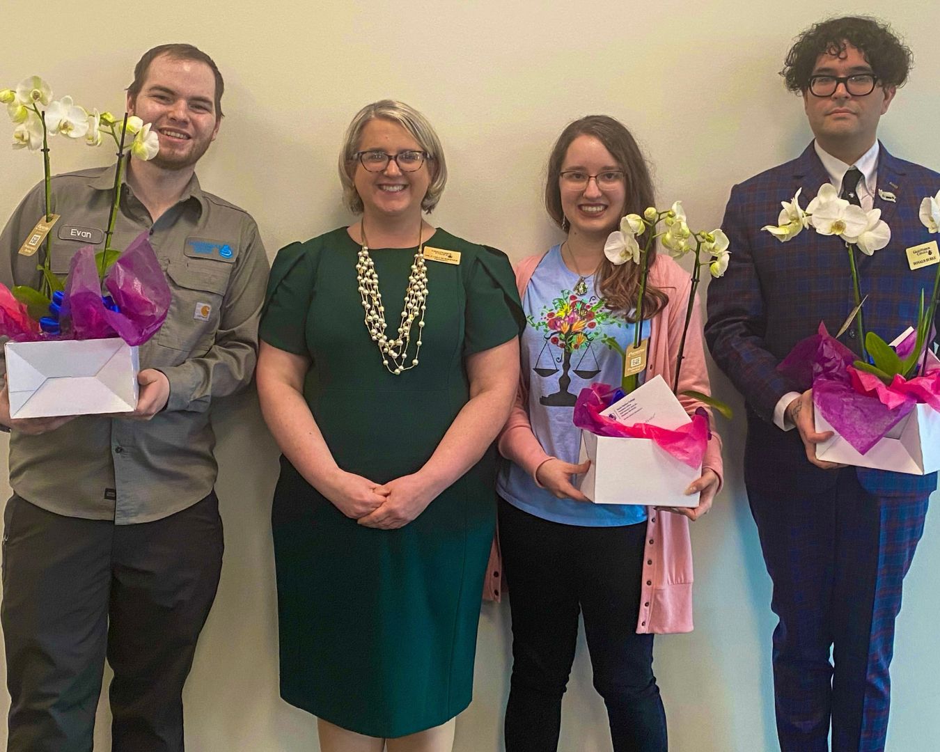 The three awarded faculty members stand with Dr. Carli Schiffner. In their arms is a box with two white blooming orchids and their congratulations letter each. 