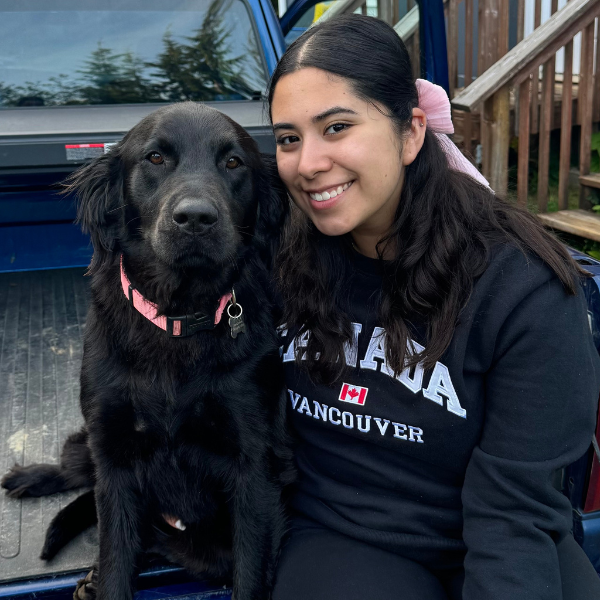 Arm wrapped around a fluffy black lab, Gladis smiles for the camera in a truck bed. 