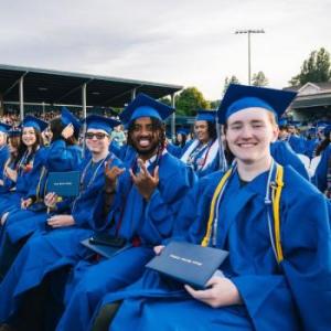 A row of seated graduates smile while holding their diplomas for the commencement ceremony.