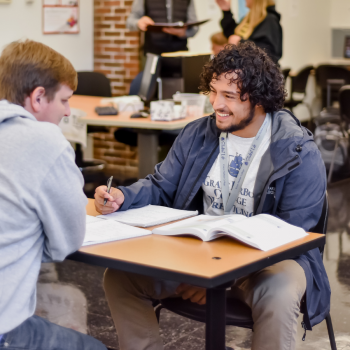 Two students sitting at a desk looking over some homework.