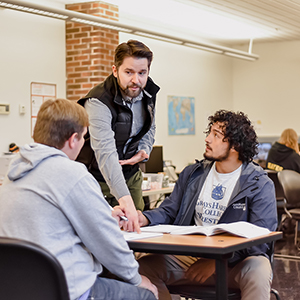 An instructor helping two students that are sitting at a desk